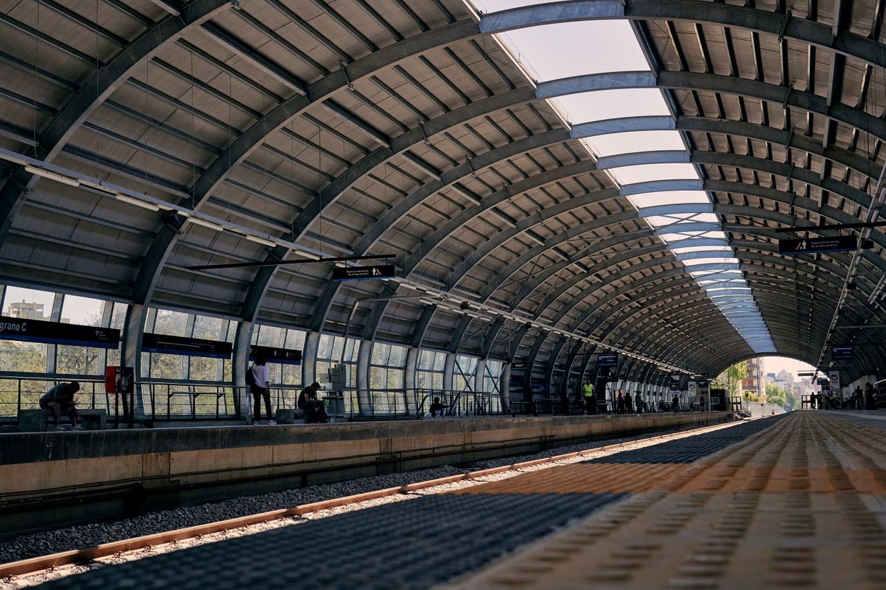 Home Modern railway station platform with curved steel roof and waiting passengers.