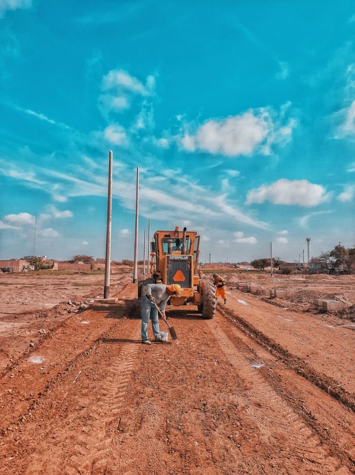 Men working at a construction site with heavy machinery on a sunny day.